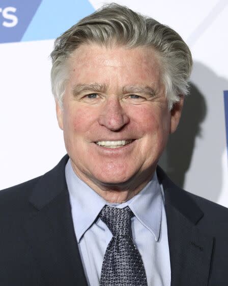 Treat Williams with gray combed hair is smiling while wearing a black suit with a light blue shirt and gray tie.