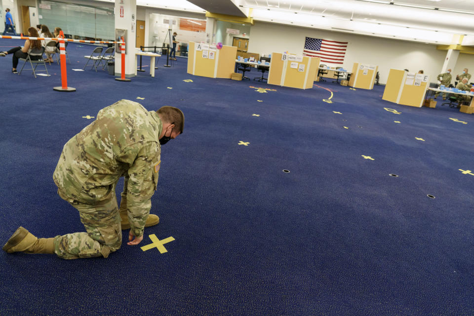 Rhode Island Army National Guard Staff Sgt. Andrew Bates pulls up tape marking a line at a coronavirus mass-vaccination site at the former Citizens Bank headquarters in Cranston, R.I., Thursday, June 10, 2021. The U.S. is confronted with an ever-growing surplus of COVID-19 vaccines, looming expiration dates and stubbornly lagging demand at a time when the developing world is clamoring for doses to stem a rise in infections. (AP Photo/David Goldman)