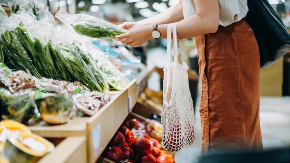 Woman shopping for fresh groceries in supermarket. She is shopping with a cotton mesh eco bag.