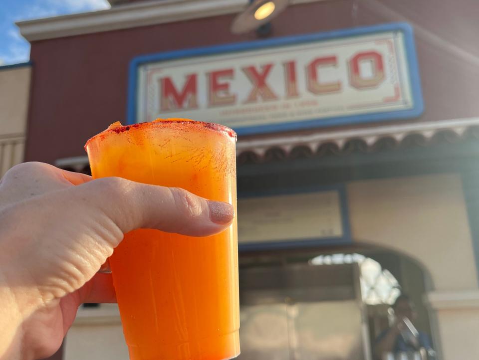 hand holding a cocktail in front of a mexico booth in epcot's world showcase at disney world