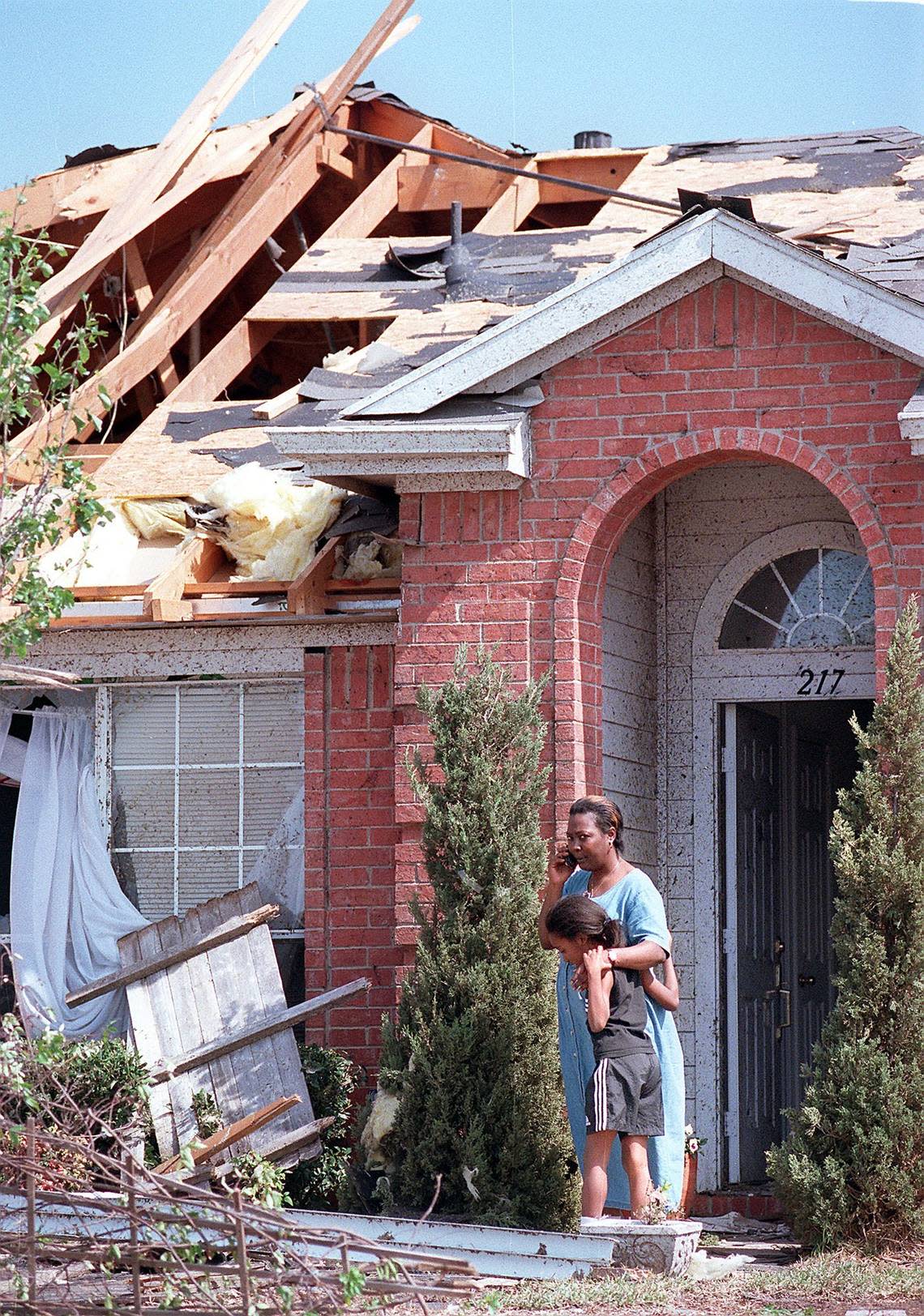 A woman hugs a child while speaking on the phone in front of their house in South Arlington after the March 28, 2000, tornado.