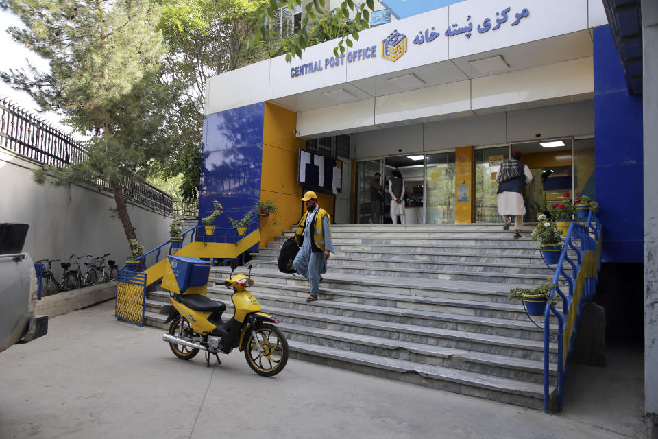 A postman walks in front of The Afghan Post office in the city of Kabul, Afghanistan, Wednesday, July 3, 2024. In parts of Afghanistan where there are no street names or house numbers, utility companies and their customers have adopted a creative approach for connecting. They use mosques as drop points for bills and cash, a "pay and pray" system. (AP Photo/Siddiqullah Alizai)