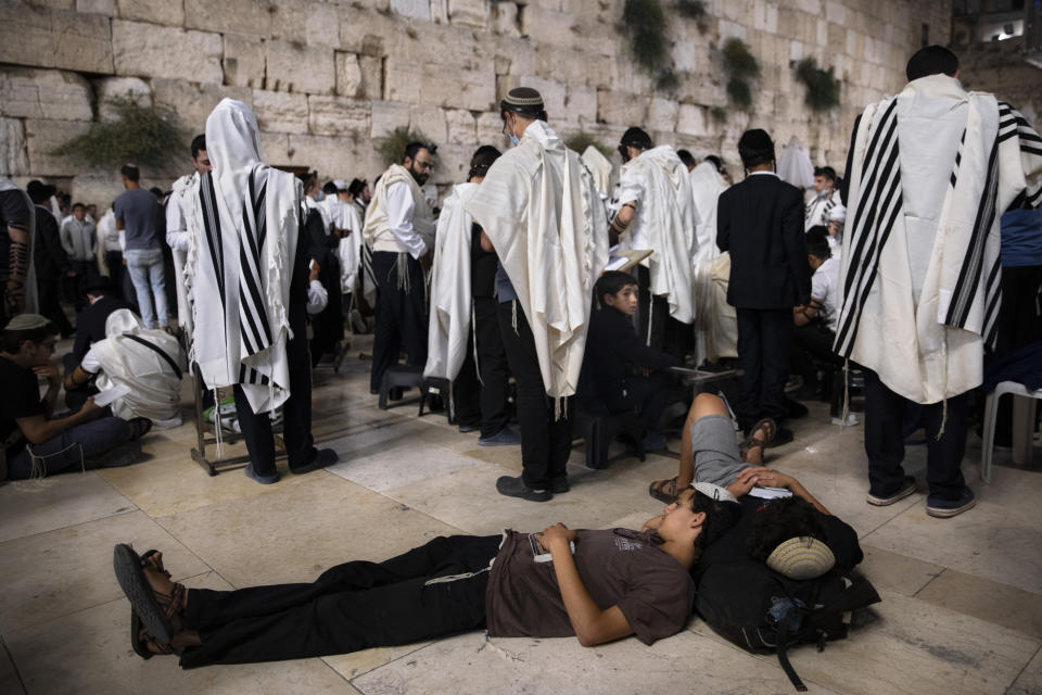 Ultra-Orthodox Jewish men pray as others sleep during the mourning ritual of Tisha B'Av (Ninth of Av) fasting and a memorial day, commemorating the destruction of ancient Jerusalem temples at the Western Wall, the holiest site where Jews can pray in the Old City of Jerusalem, Sunday, July 18, 2021. (AP Photo/Oded Balilty)