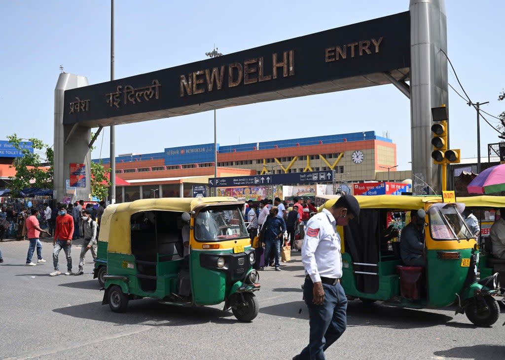 A traffic policeman, people and vehicles make their way near an entrance of the New Delhi Railway (AFP via Getty Images)