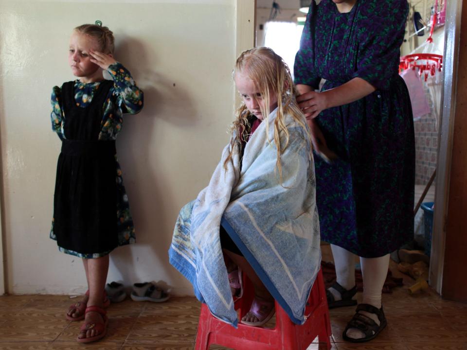 Mennonite children take turns getting their hair braided by their mother, which they do once a week.