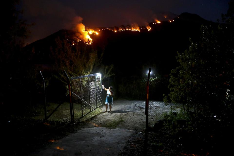 In this Tuesday, Jan. 24, 2017 photo, a woman closes a gate on her land as wildfires rage on a nearby mountain in Cajon del Maipo, on the outskirts of Santiago, Chile. Chile is suffering one of its worst fire diasters in history. The fires have outpaced local ability to put them out, forcing Chile to request international aid. (AP Photo/Esteban Felix)