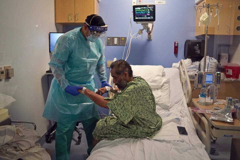 Physical therapist Daniel Lumbera helps a COVID-19 patient sit up on his bed at St. Joseph Hospital in Orange, Calif. Thursday, Jan. 7, 2021. The state's hospitals are trying to prepare for the possibility that they may have to ration care for lack of staff and beds — and hoping they don't have to make that choice, as many hospitals strain under unprecedented caseloads. (AP Photo/Jae C. Hong)