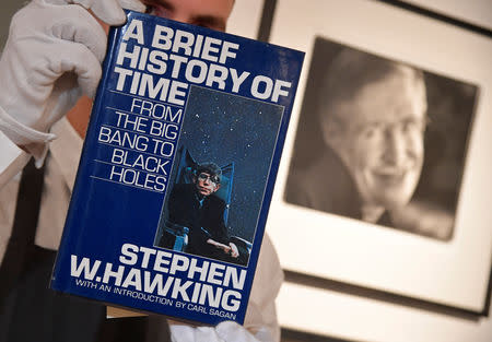FILE PHOTO: Fine-art handler Tom Richardson poses with a copy of A Brief History of Time which, has a thumb-print inside by author British theoretical physicist Stephen Hawking, ahead of an auction of items from Hawkinsg' personal estate at Christie's in London, Britain October 30, 2018. REUTERS/Toby Melville/File Photo