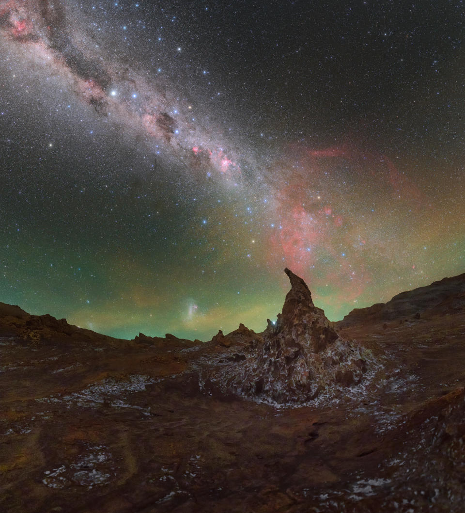 above rock formations in the desert, thousands of stars surround the white, wispy glow of the milky way stretching like a belt across the sky