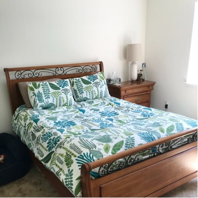 Bed with patterned bedding and wooden headboard in a bedroom, furniture visible