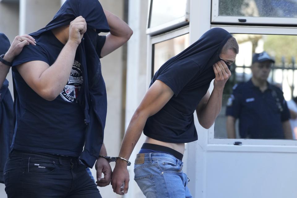Soccer fans covering their faces, most of them from Croatia, are escorted by police as they leave the Athens Police Headquarters, Greece, Wednesday, Aug. 9, 2023. Ninety-four fans of Croatia's Dinamo Zagreb are appearing in court this morning for a preliminary hearing over Monday night's fan violence that left a fan of Greece's AEK dead and another eight people injured. (AP Photo/Petros Giannakouris)
