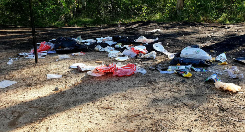 Garbage dumped at Noosa North Shore Beach Campground including plastic bags and paper plates. 