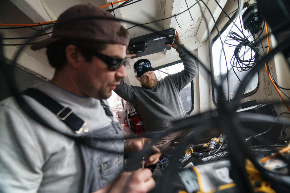 Mark Hager, right, and Anthony Lucia, install the electronics for a camera aboard the Sabrina Maria fishing boat, in Gloucester, Mass., May 11, 2022. Hager's Maine-based startup, New England Maritime Monitoring, is one of a bevy of companies seeking to help commercial vessels comply with new federal mandates aimed at protecting dwindling fish stocks. But taking the technology overseas, where the vast majority of seafood consumed in the U.S. is caught, is a steep challenge. (AP Photo/David Goldman)