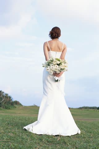 <p>Getty</p> Stock photo of a bride turned with her back to the camera holding flowers behind her