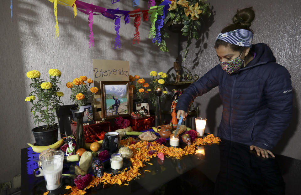 Karen Valencia, lights candles on a Day of the Dead altar for her father Jose Valencia, a male nurse who died from symptoms related to COVID-19, at their home in Mexico City, Sunday, Nov. 1, 2020. The weekend holiday isn't the same in a year so marked by death in a country where more than 90,000 people have died of COVID-19, many cremated rather than buried and with cemeteries forced to close. (AP Photo/Eduardo Verdugo)