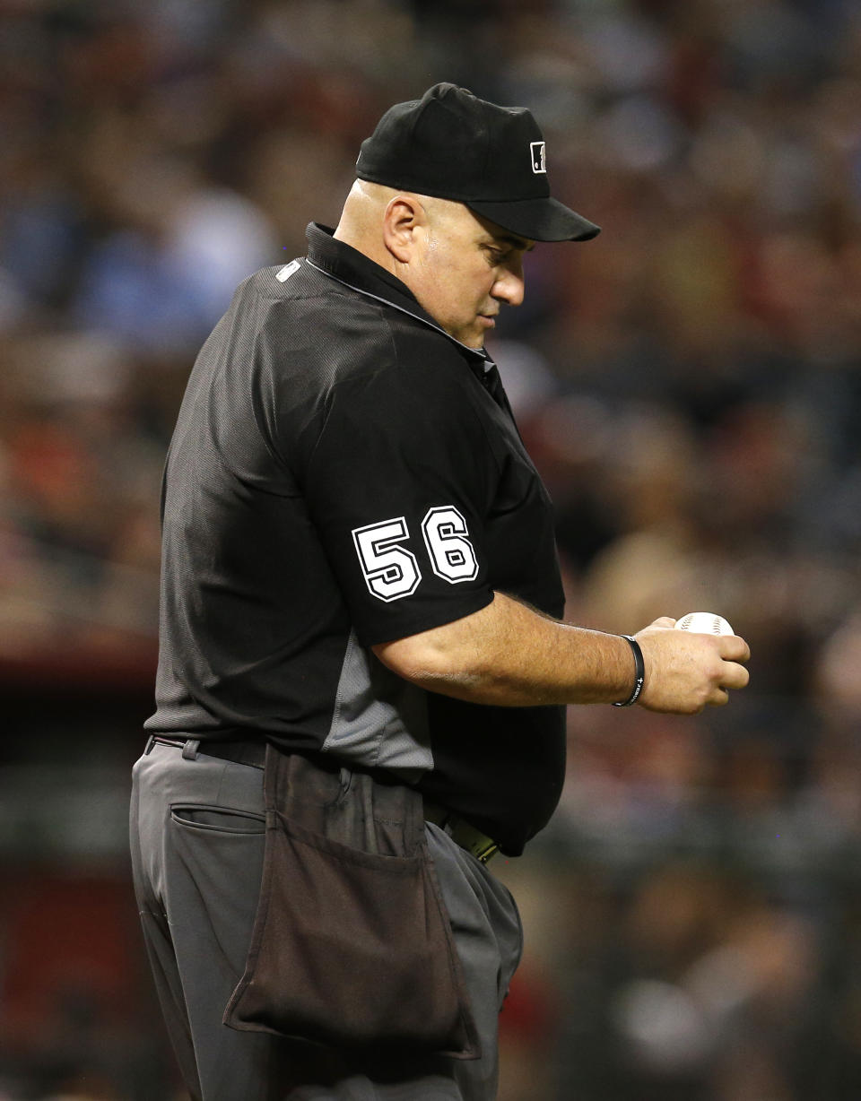 FILE - Umpire Eric Cooper (56) inspects the ball in the sixth inning during a baseball game between the Arizona Diamondbacks and the Colorado Rockies in Phoenix, in this Friday, Sept. 21, 2018, file photo. Pitchers will be ejected and suspended for 10 games for using illegal foreign substances to doctor baseballs in a crackdown by Major League Baseball that will start June 21. The commissioner’s office, responding to record strikeouts and a league batting average at a more than half-century low, said Tuesday, June 15, 2021, that major and minor league umpires will start regular checks of all pitchers, even if opposing managers don’t request inspections.(AP Photo/Rick Scuteri, File)