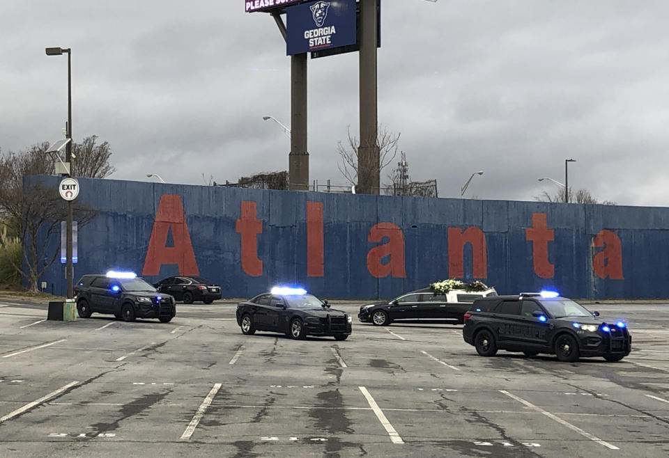 The hearse, back right, carrying the casket of Hank Aaron leaves the parking lot after making a loop of the old stadium site Wednesday, Jan. 27, 2021, in Atlanta. A retaining wall for the former ballpark is in the background. After a nearly three-hour funeral service that featured two former presidents, a long-time baseball commissioner and a civil rights icon, the hearse carrying Aaron's body detoured off the road bearing his name to swing through the former site of Atlanta-Fulton County Stadium. (AP Photo/Paul Newberry)