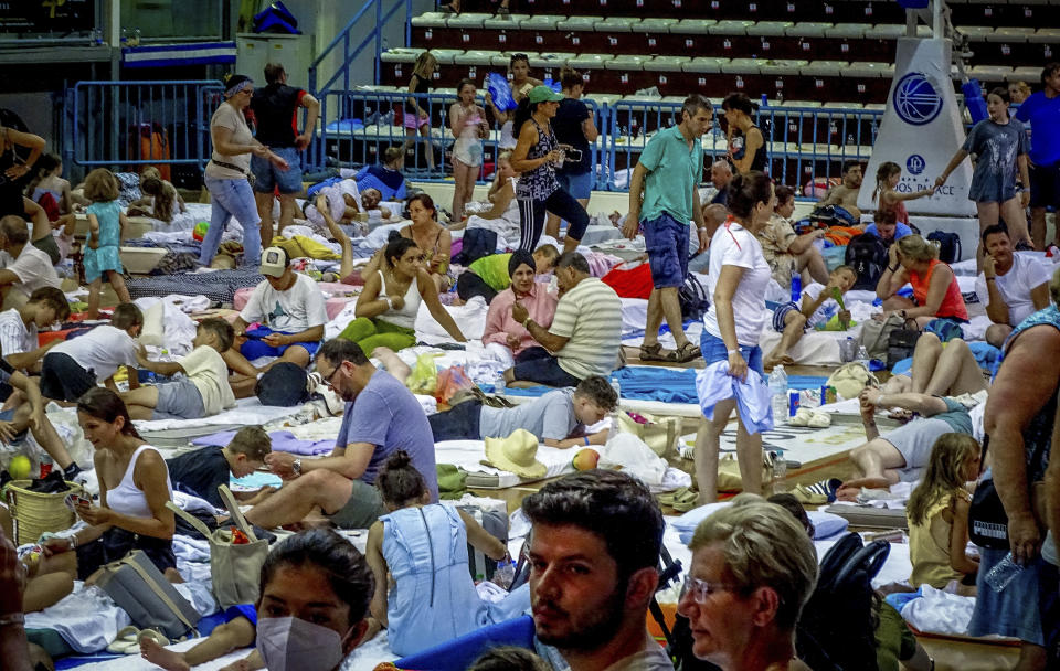 Evacuees sit inside a stadium following their evacuation during a forest fire on the island of Rhodes, Greece, Sunday, July 23, 2023. Some 19,000 people have been evacuated from the Greek island of Rhodes as wildfires continued burning for a sixth day on three fronts, Greek authorities said on Sunday. (Argyris Mantikos/Eurokinissi via AP)