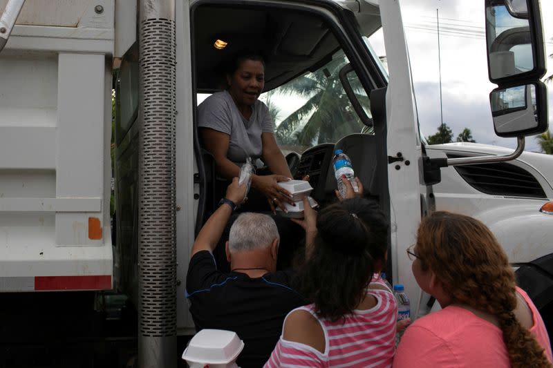 People hand bottles of water and containers with free food to a woman in a truck after an earthquake in Yauco
