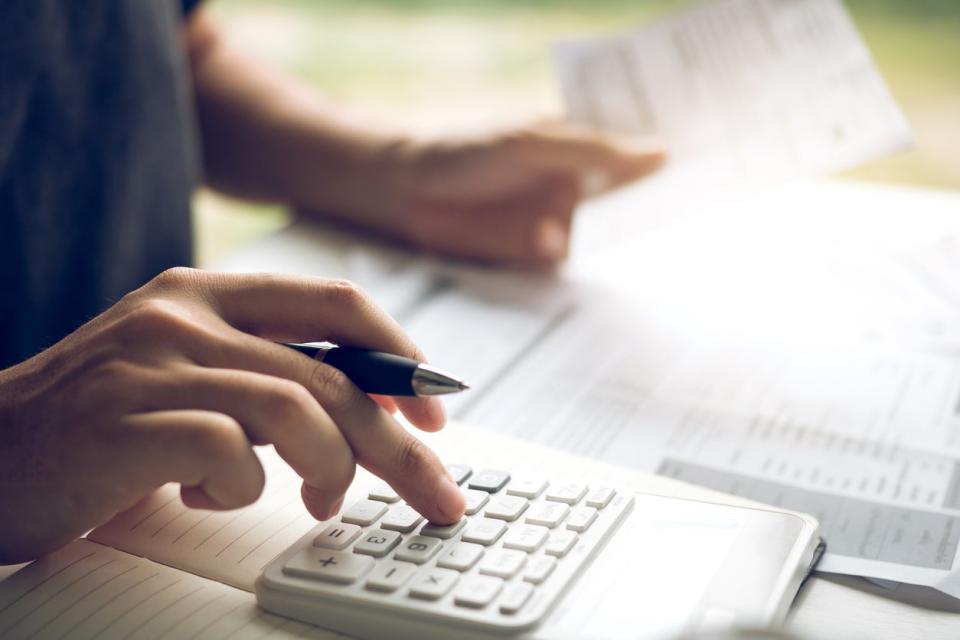 A close up of a person's hand using a calculator while the other holds up a document. 