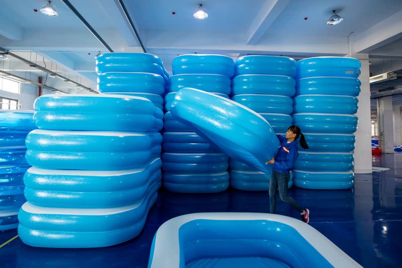 A worker piles up newly made inflatable swimming pools at a workshop of a company manufacturing sports equipment in Haian, Jiangsu