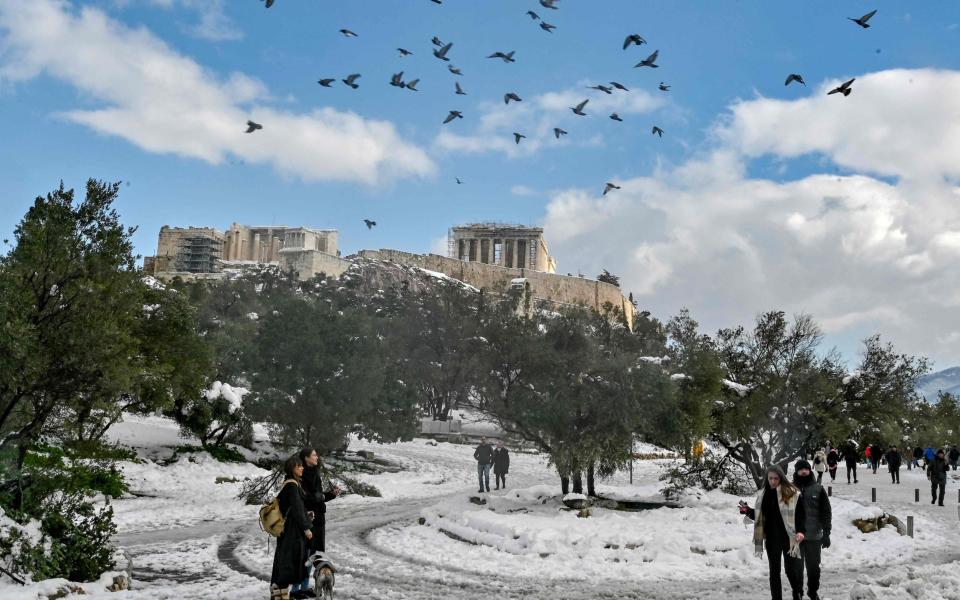 Pedestrians walk in the snow below the Acropolis in Athens - LOUISA GOULIAMAKI /AFP