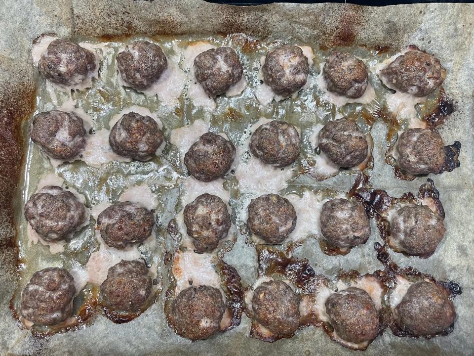 a tray lined with cooked meatballs and meat grease