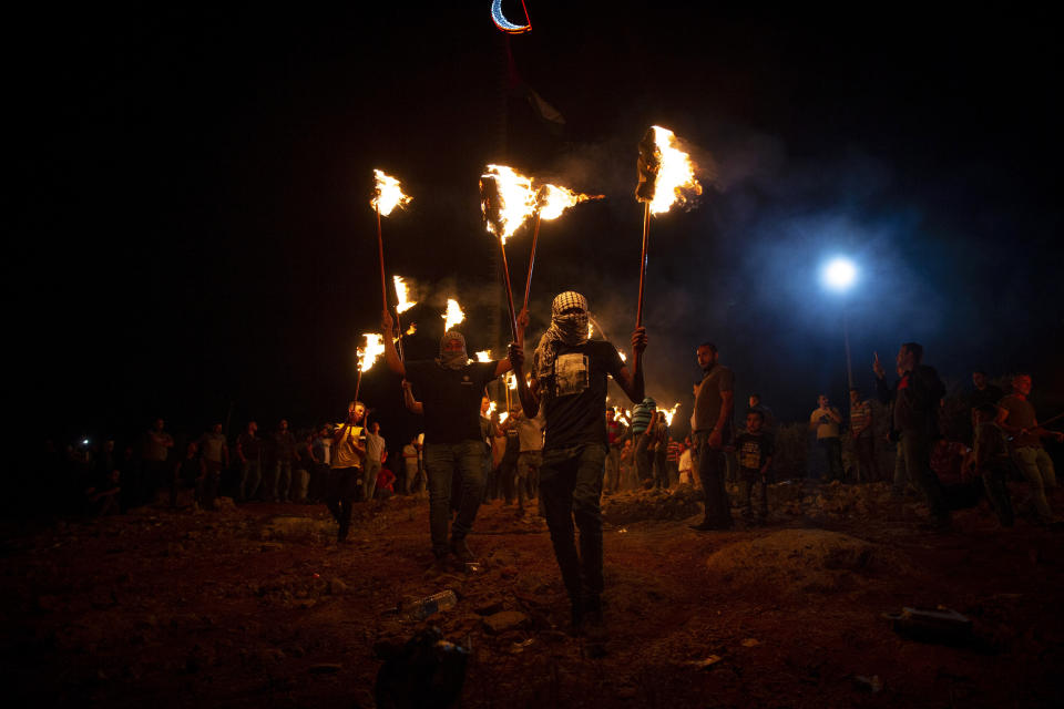 Palestinian demonstrators march with torches during a demonstration against the West Bank Jewish settlement outpost of Eviatar that was rapidly established last month, at the Palestinian village of Beita, near the West Bank city of Nablus, Sunday, June 27, 2021. The Palestinians say it was established on their farmland and fear it will grow and merge with other large settlements in the area. (AP Photo/Majdi Mohammed)