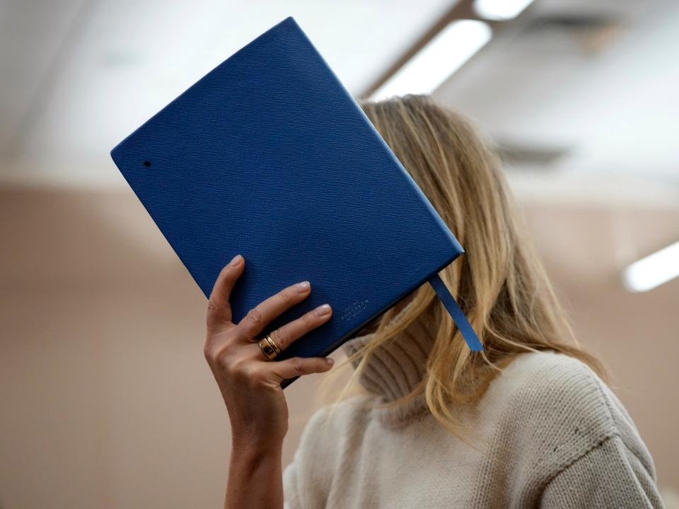 Actress Gwyneth Paltrow shields her face with a blue notebook as she exits a courtroom.