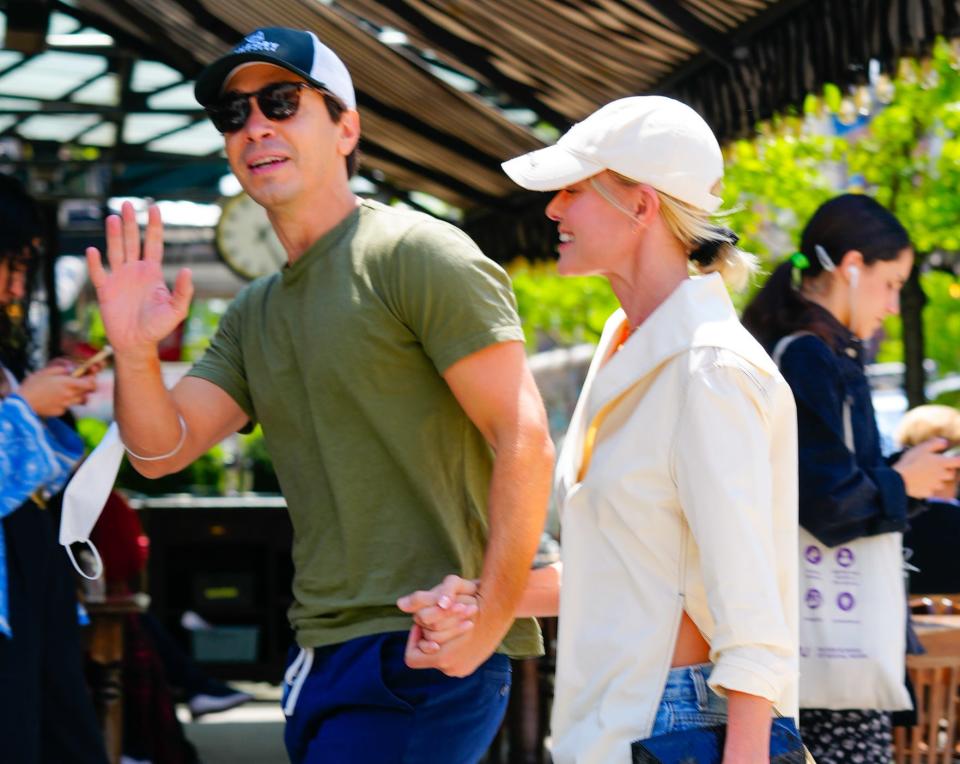 Kate and Justin hold hands and wave while walking down the street