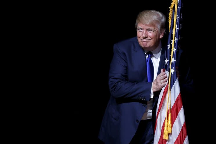 Trump hugs a U.S. flag as he takes the stage for a campaign town hall meeting in Derry, N.H., Aug. 19, 2015. (Brian Snyder/Reuters)