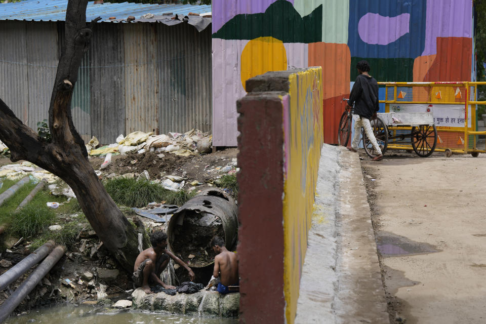 Laborers wash their clothes in sewage water under a bridge, newly painted and decorated in preparation for the G20 summit, in New Delhi, India, Thursday, Aug. 24, 2023. As India gears up to host the annual gathering of the Group of 20 industrialized and developing nations, the capital city is undergoing an elaborate makeover. But for many street vendors and shantytowns dotting the city, the beautification of New Delhi has meant displacement and loss of livelihoods. (AP Photo/Manish Swarup)