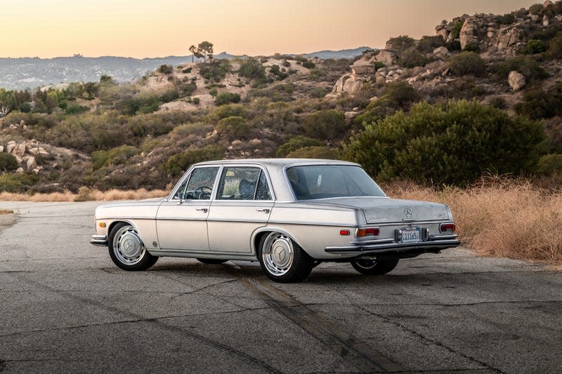 A silver 1971 Mercedes-Benz 300SEL parked in front of rocks, rear three quarter view