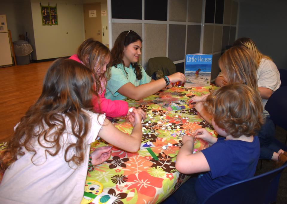 Jaclyn Hildebrand, an Adrian College junior and a student in the teacher education program, third from left, assisted quite a few younger children with making seashell necklaces and bracelets Wednesday, Dec. 6, 2023, during a beach themed event held at the Adrian District Library and coordinated by the TED students at Adrian College.