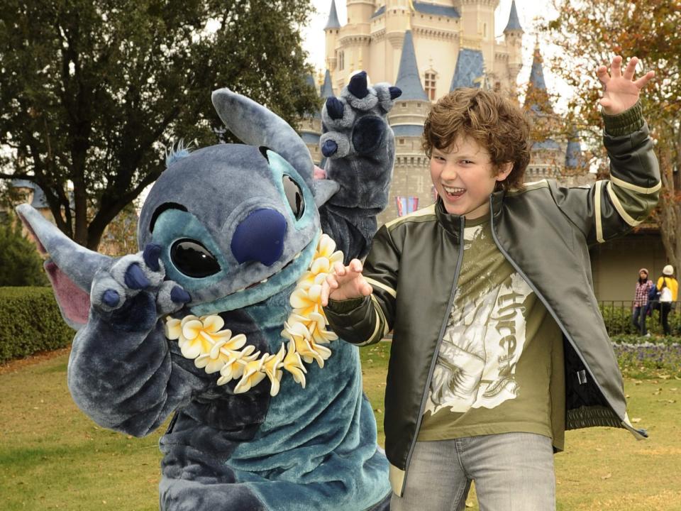 A life-size soft mascot costume of a blue alien and a young boy both with their arms up and growling faces.