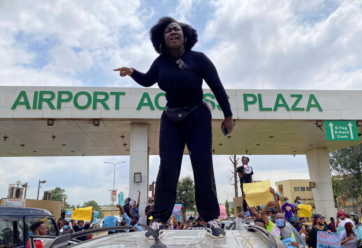 A demonstrator stands atop a vehicle and shouts slogans as others carry banners while blocking a road leading to the airport in Lagos on Oct. 12, 2020.