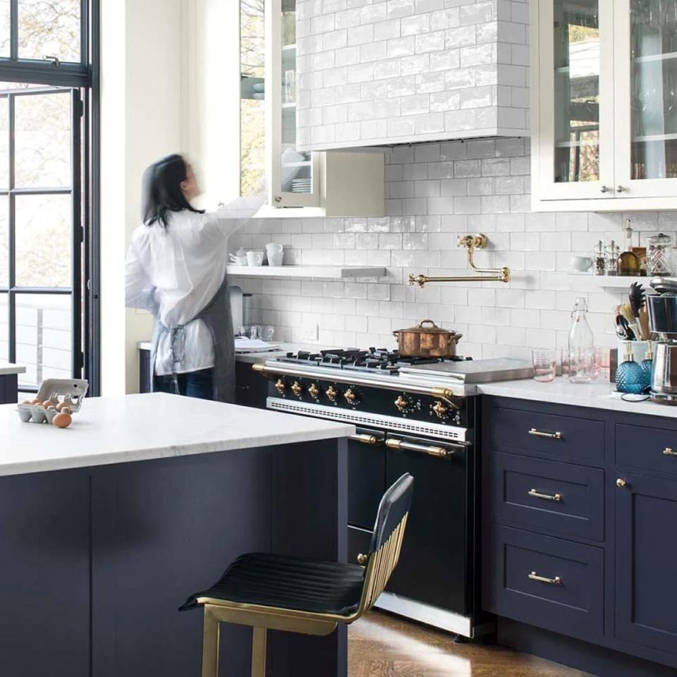 Woman in kitchen that has white subway tile and dark blue Hale Navy-painted cabinets.