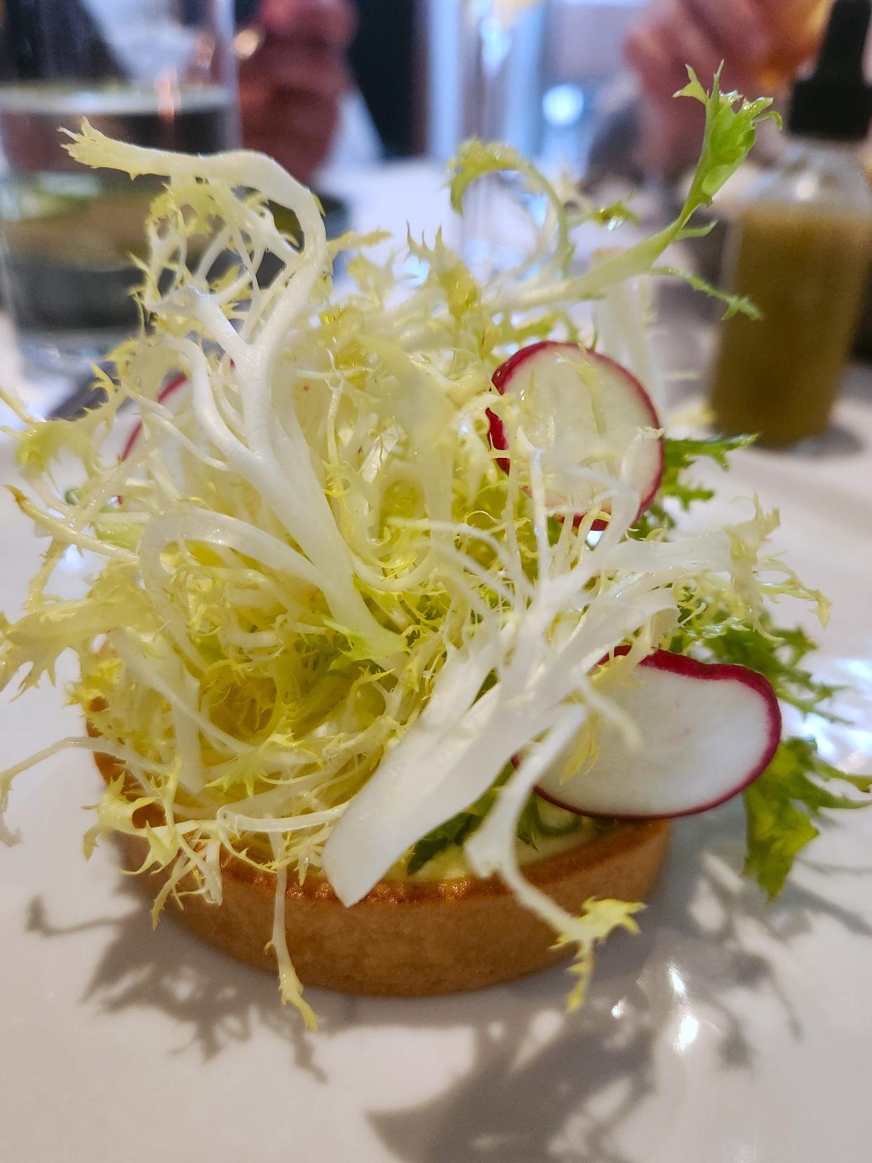 A goat cheese and caramelized onion tarte is garnished with frisee and radish slices at Cosmos Bistro on Thursday, May 3, 2024.