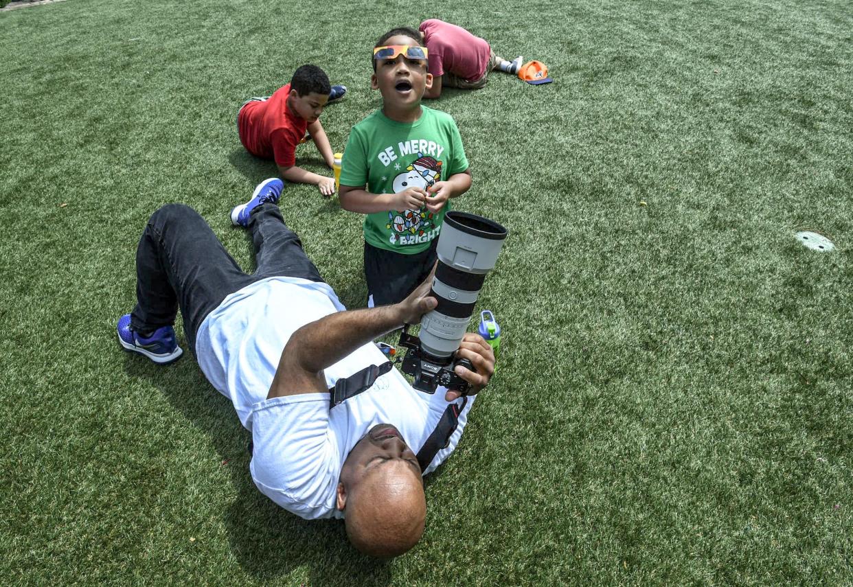 Jayde Day, middle, of Augusta, Georgia, checks out the sun with proper solar eclipse glasses with their father Dion Day taking photos with a photography filter, at Falls Park during a solar eclipse with viewers in Greenville, S.C. Monday, April 8, 2024.