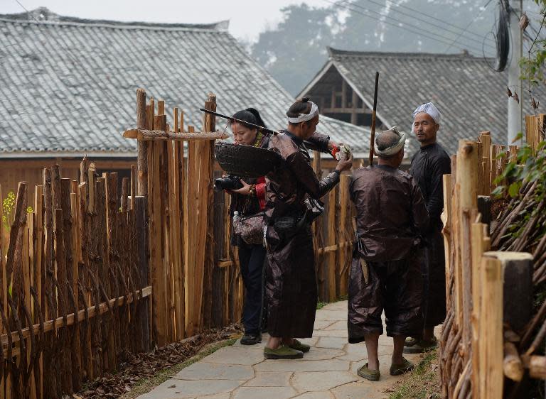 A tourist walks past members of the Miao minority group in Biasha Village, Guizhou Province on February 4, 2014