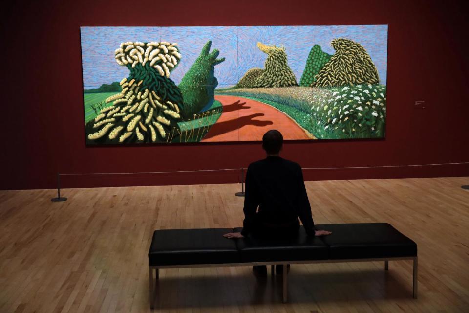 A Tate representative poses for photographs next to British artist David Hockney's "May Blossom on the Roman Road" during a photocall to promote the largest-ever retrospective of his work at Tate Britain gallery in London, Monday, Feb. 6, 2017. The exhibition, which opens to the public from February 9 and runs until May 29, celebrates the 79-year-old's achievement in painting, drawing, photography and video. (AP Photo/Matt Dunham)