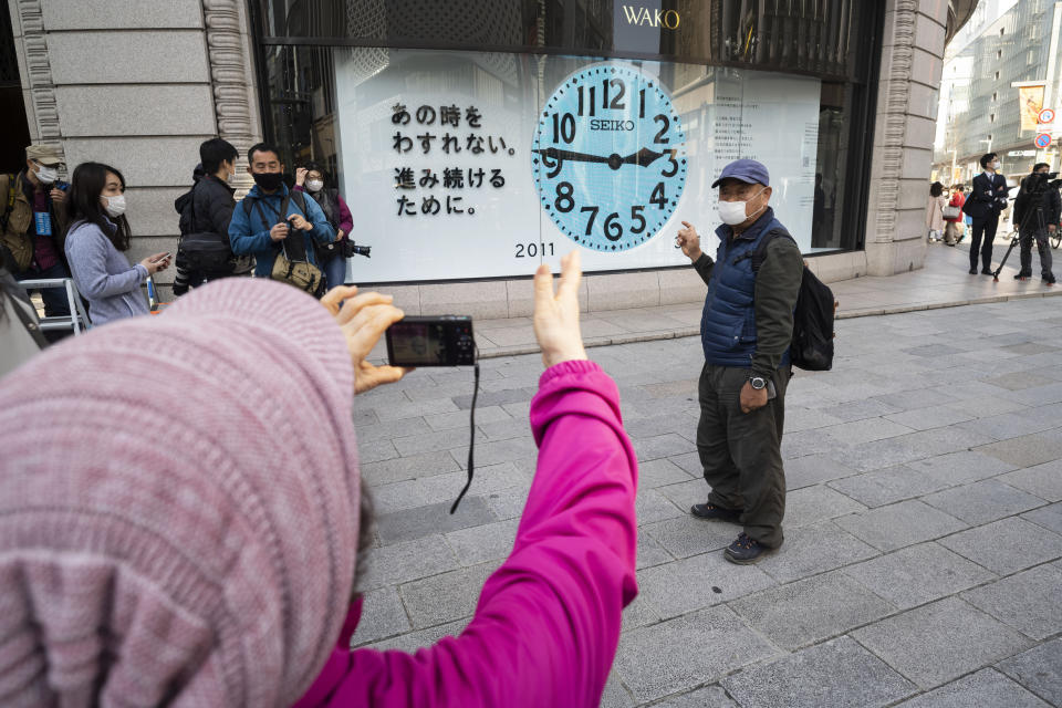 A woman takes a photo of her husband in front of a clock that shows 2:46 p.m. to commemorate the 2011 earthquake that hit the northeastern Japan, before the 10th anniversary to pay tribute to the victims in Tokyo Thursday, March 11, 2021. Japan is marking the 10th anniversary Thursday of the earthquake, tsunami and nuclear disaster that hit the northeastern region. (AP Photo/Hiro Komae)