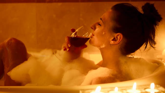 Girl in the bath having a glass of red wine,, candle lit.