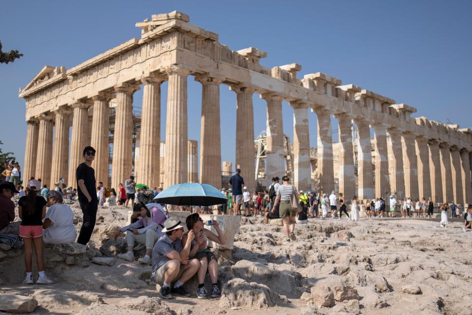 Tourists shelter from the heat under an umbrella in front of Parthenon temple at the Acropolis hill in Athens, Greece, on July 13, 2023.