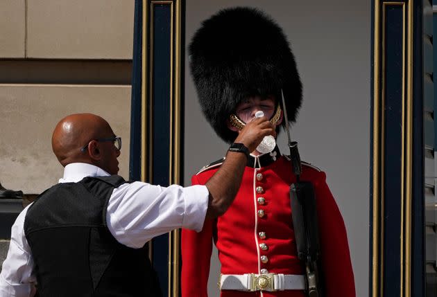 A police officer gives water to a British soldier wearing a traditional bearskin hat, on guard duty outside Buckingham Palace, during hot weather in London on Monday. (Photo: via Associated Press)