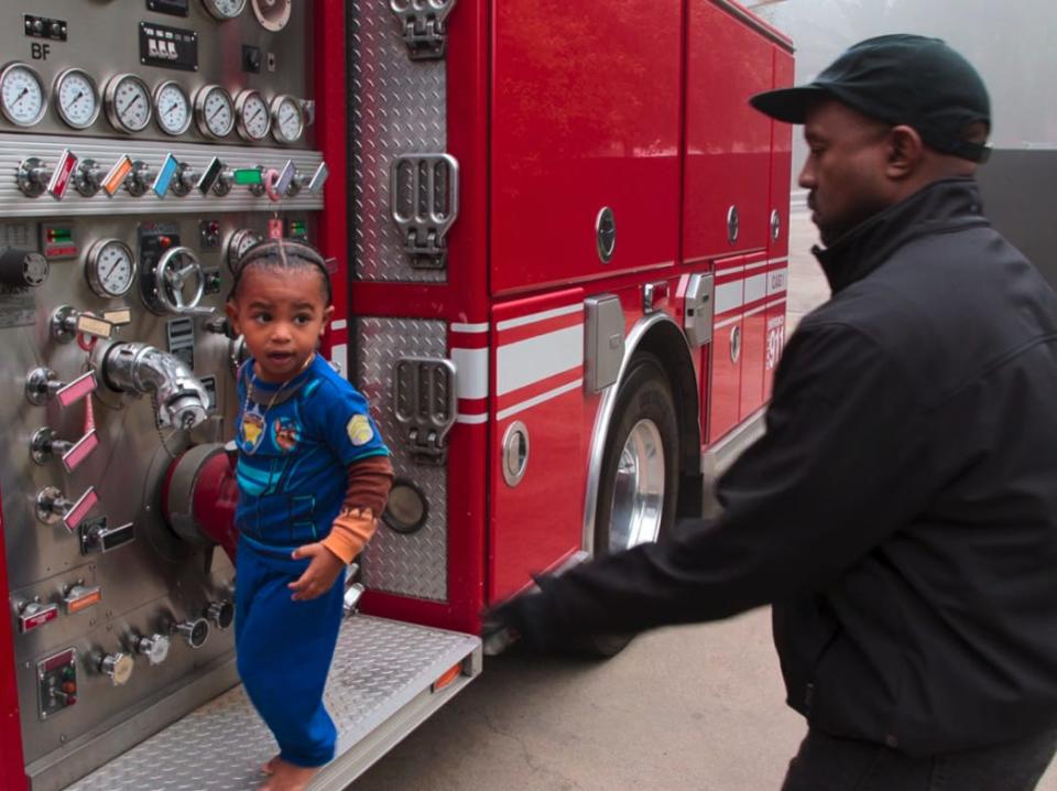 kanye west and his son, who is standing on a platform on a fire truck near a number of valves and openings