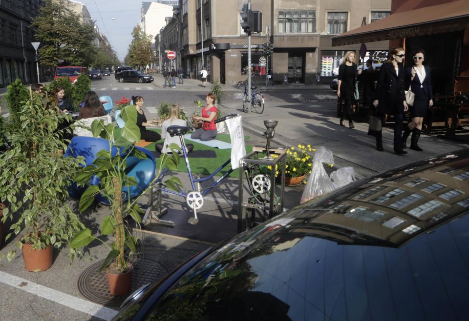 Pedestrians walk past people participating in a PARK(ing) Day event in Riga