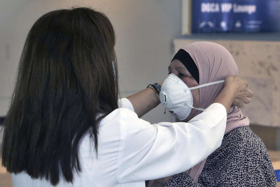 A healthcare worker adjusts the mask of a passenger who is departing the Rafik Hariri International Airport in Beirut, Lebanon, Wednesday, July 1, 2020. Beirut's airport is partially reopening after a three-month shutdown and Lebanon's cash-strapped government is hoping that thousands of Lebanese expatriates will return for the summer, injecting dollars into the country's sinking economy. (AP Photo/Bilal Hussein)