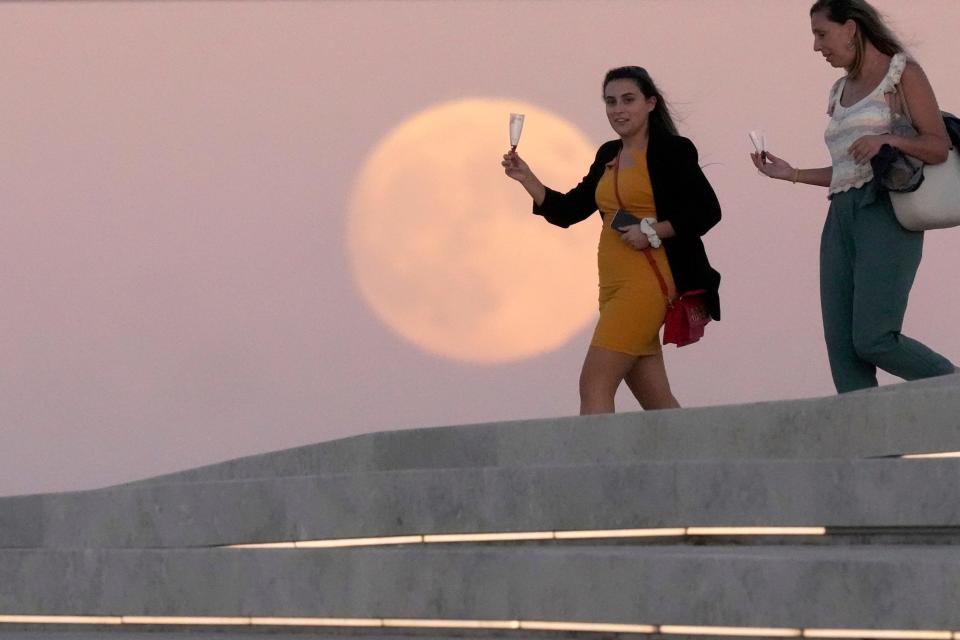 People have drinks on the roof of the Museum of Art, Architecture and Technology in Lisbon, as a full supermoon rises in the background, Thursday, Sept. 28, 2023. It's the fourth and last supermoon of the year, when a full moon appears a little bigger and brighter thanks to its slightly closer position to Earth. (AP Photo/Armando Franca)