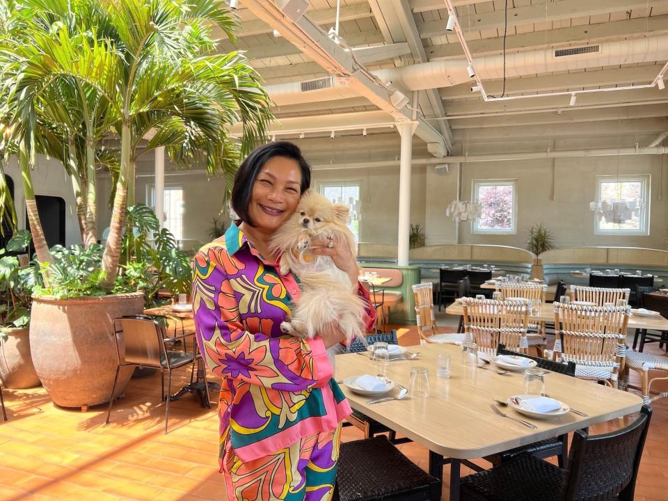 Chef Chutatip "Nok" Suntaranon wearing a matching set with a vibrant, retro print holds her Pomeranian dog TiTi in her restaurant Kalaya.